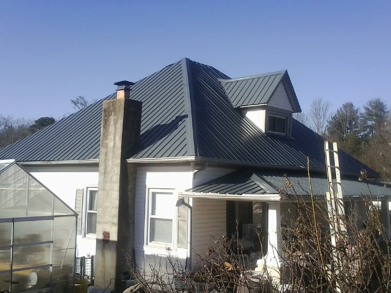 Dark blue standing seam metal roof on a white farmhouse with dormer — Slate & Tile Roof Repair by Roofing Brothers in Orlinda