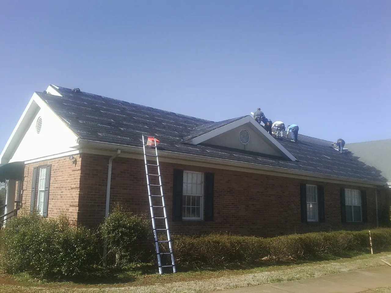 Crew tearing shingles off a brick ranch roof with a ladder set — Emergency Roof Repair work by our crew in Orlinda