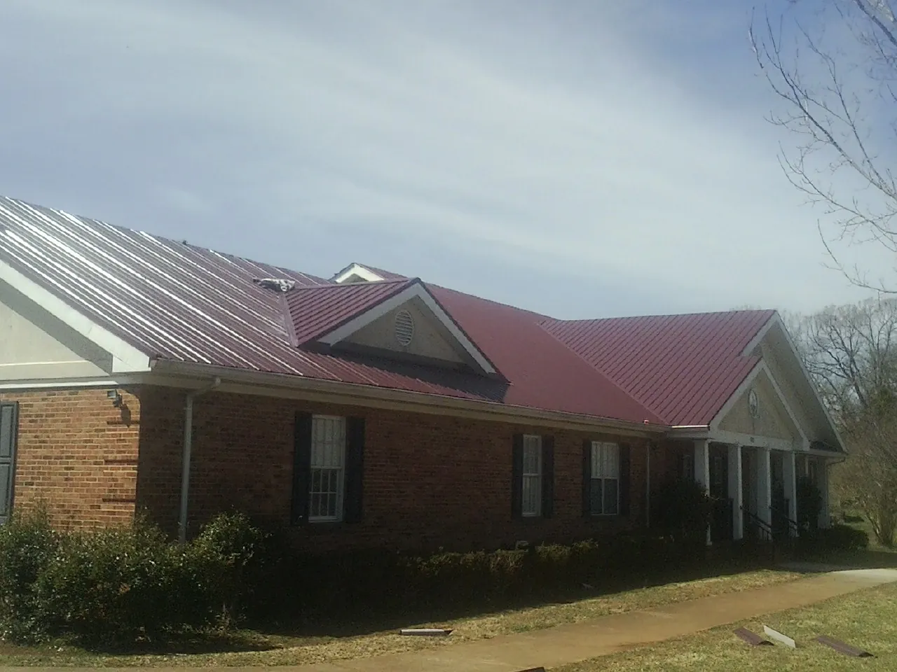 Red metal roof with gabled entries on a long brick building, from a Hail Damage Roof Repair job in Orlinda