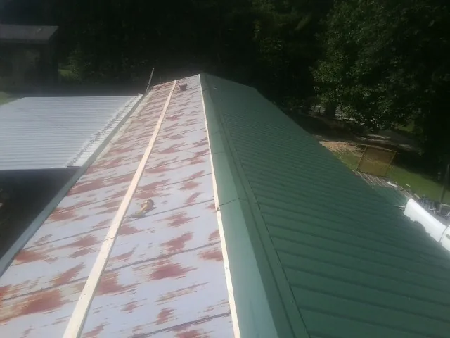 Old rusted panels beside newly installed green metal roofing — Wind Damage Roof Repair by Roofing Brothers in Orlinda
