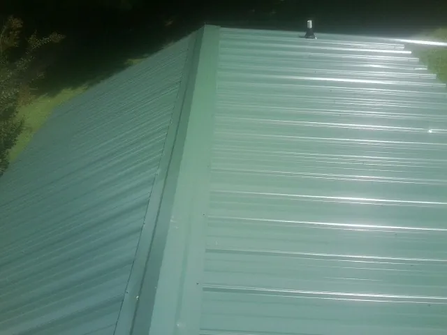 New green metal panels meeting at the ridge of a roof — Flat Roof Repair work by our crew in Orlinda