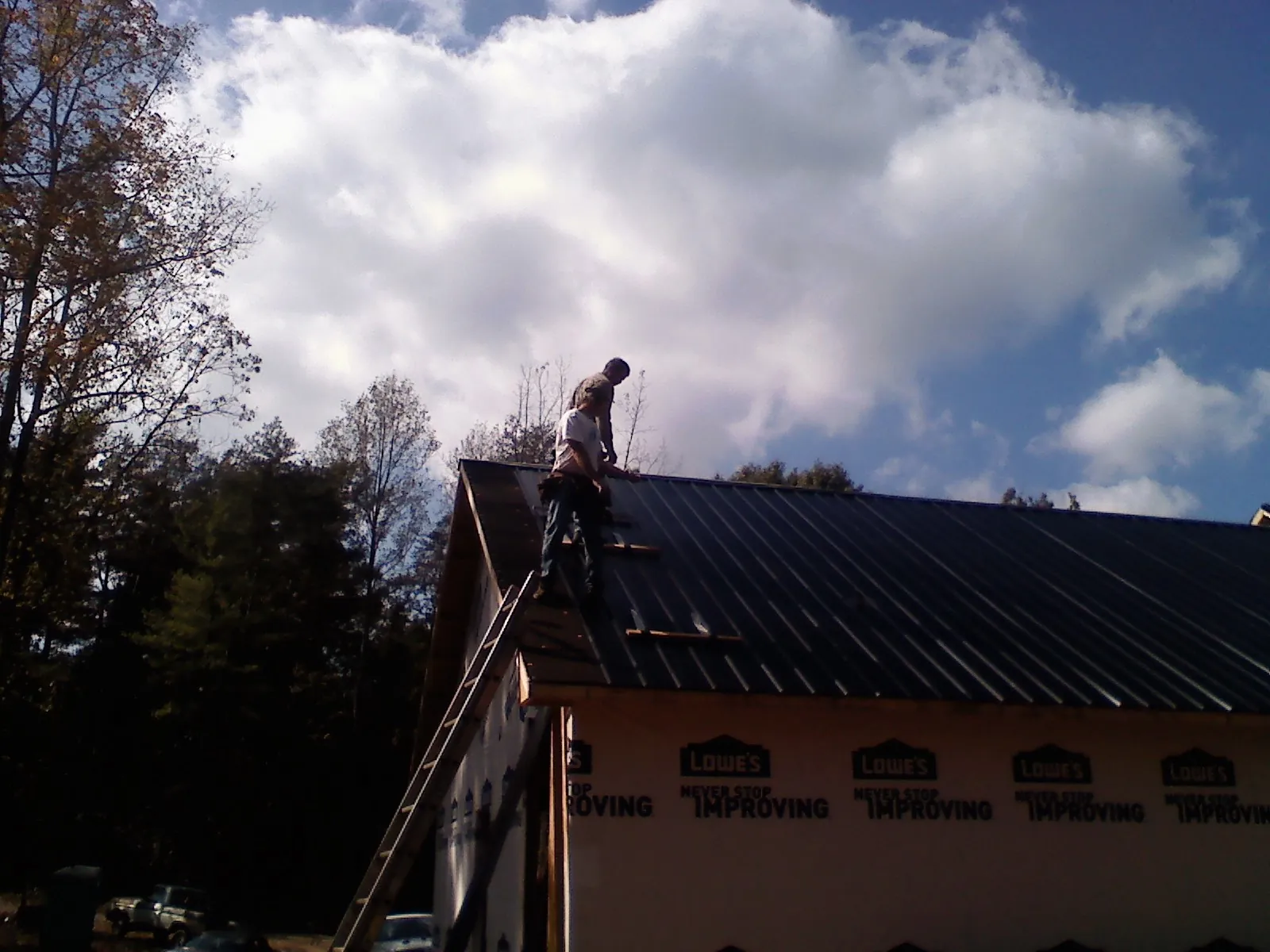 Roofer fastening dark metal panels high against a cloudy sky, from a Roof Inspection job in Orlinda
