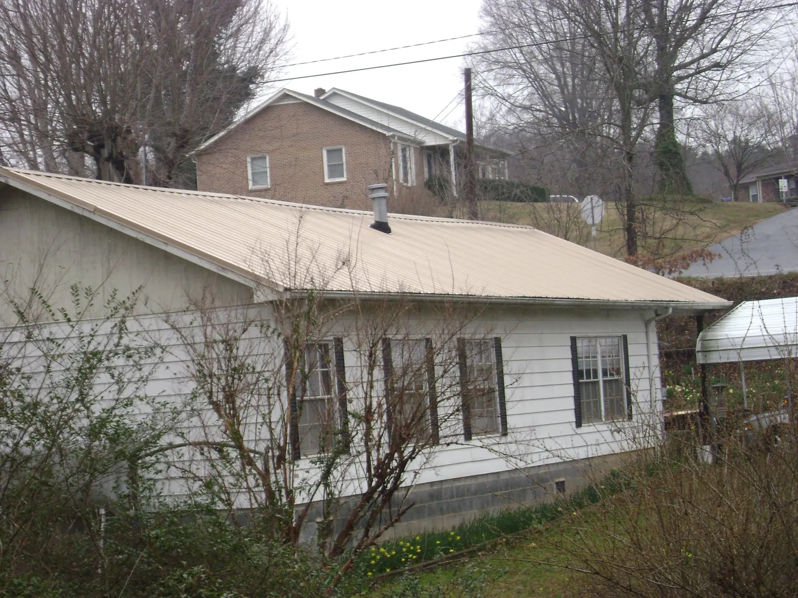 Tan metal roof on a white sided house set into a hillside — Commercial Roofing by Roofing Brothers in Orlinda